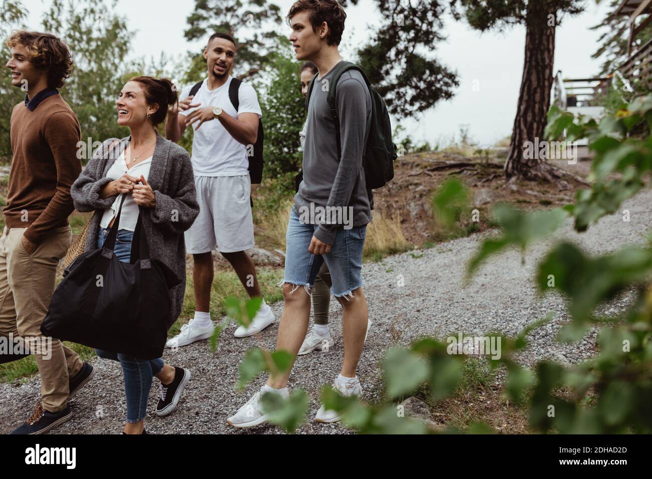 Smiling friends and family walking on footpath amidst trees during vacation Stock Photo