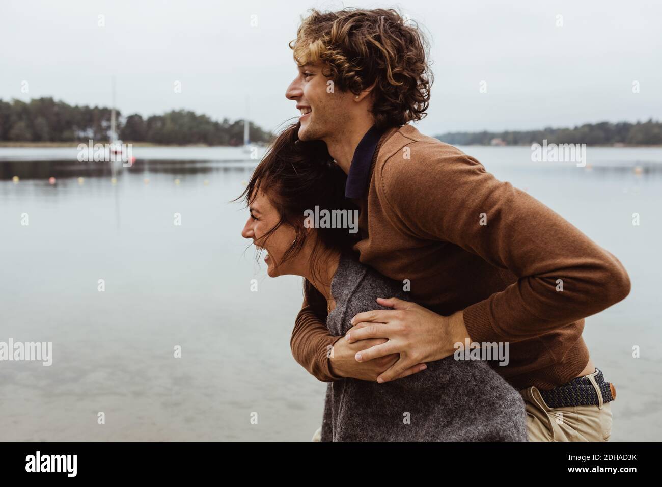 Smiling woman giving piggyback ride to male friend by sea against sky Stock Photo