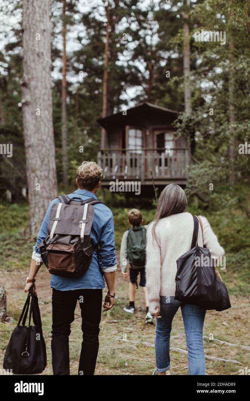 Rear view of family with bags walking towards house in forest Stock Photo