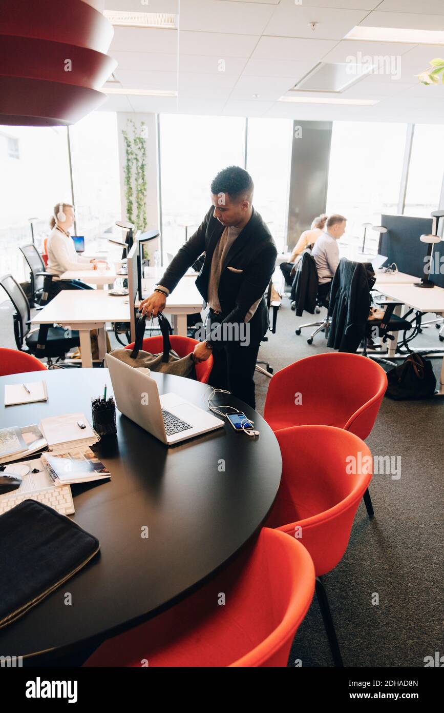Businessman holding bag on chair by desk at place of work Stock Photo