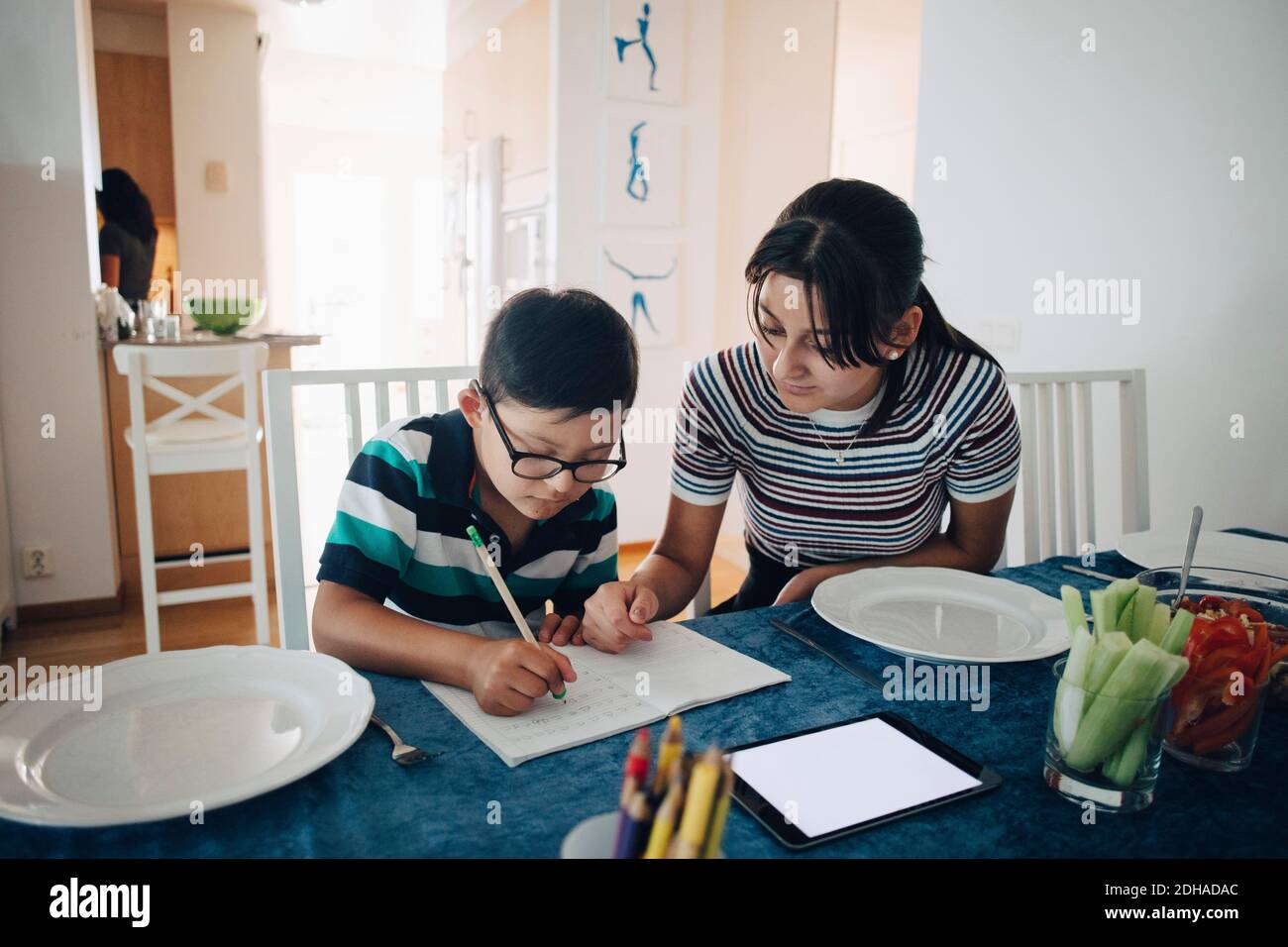Teenage girl assisting brother in homework at dining table Stock Photo