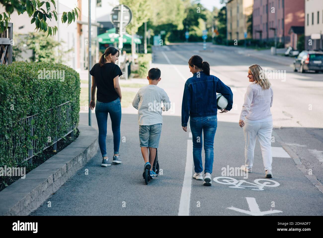 Rear view of family walking on bicycle lane street in city during sunny day Stock Photo