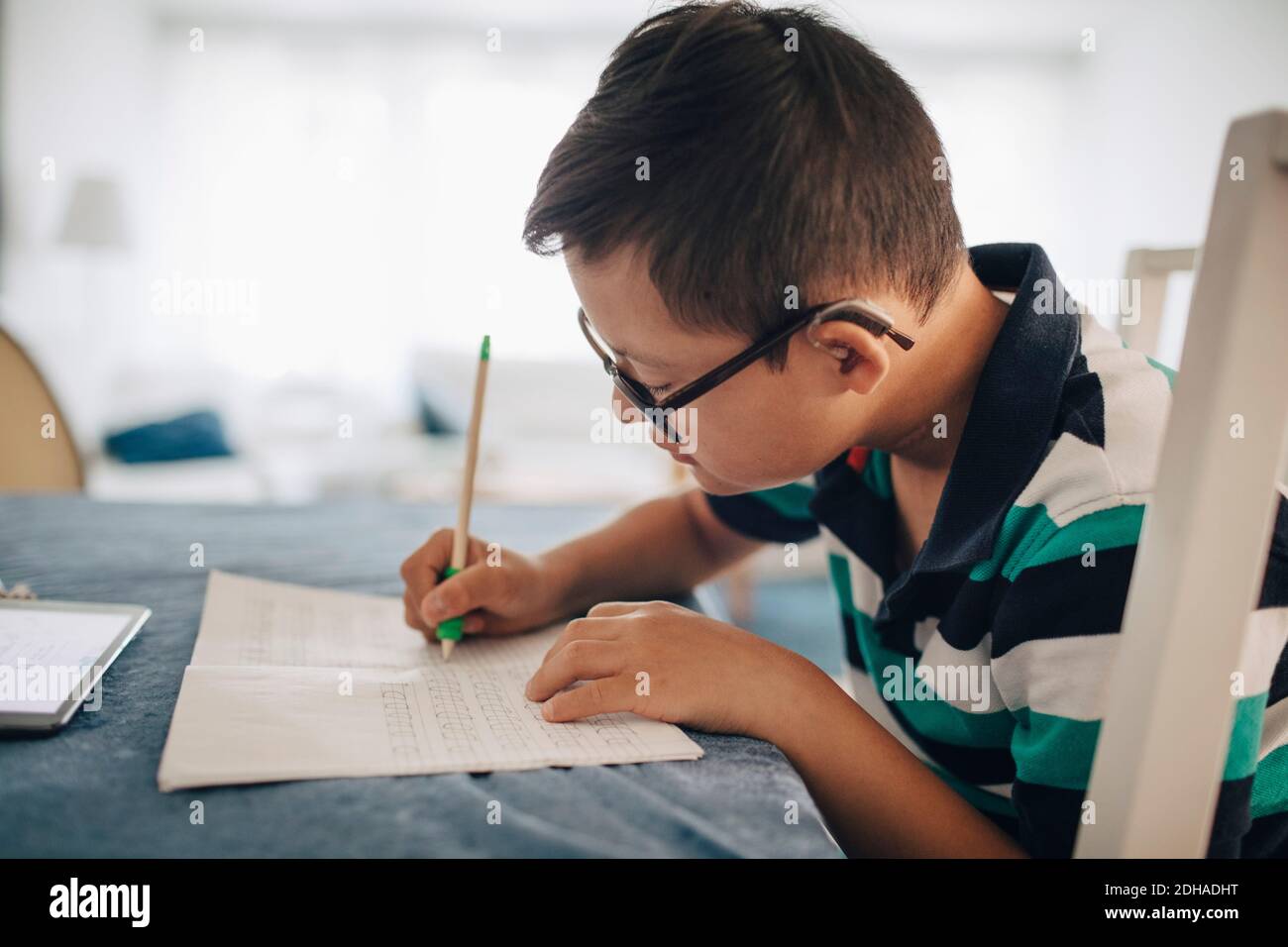 Side view of boy writing on book while sitting at table Stock Photo