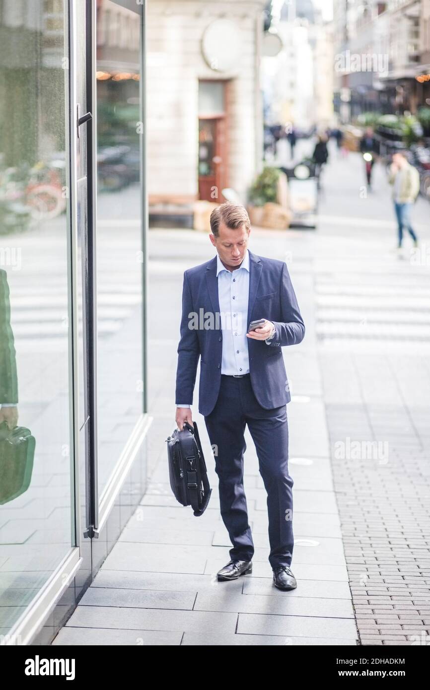 Mature businessman using smart phone while standing in city Stock Photo ...
