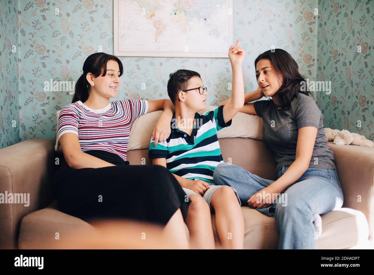 Disabled boy talking to sisters while sitting on sofa against wall at home Stock Photo