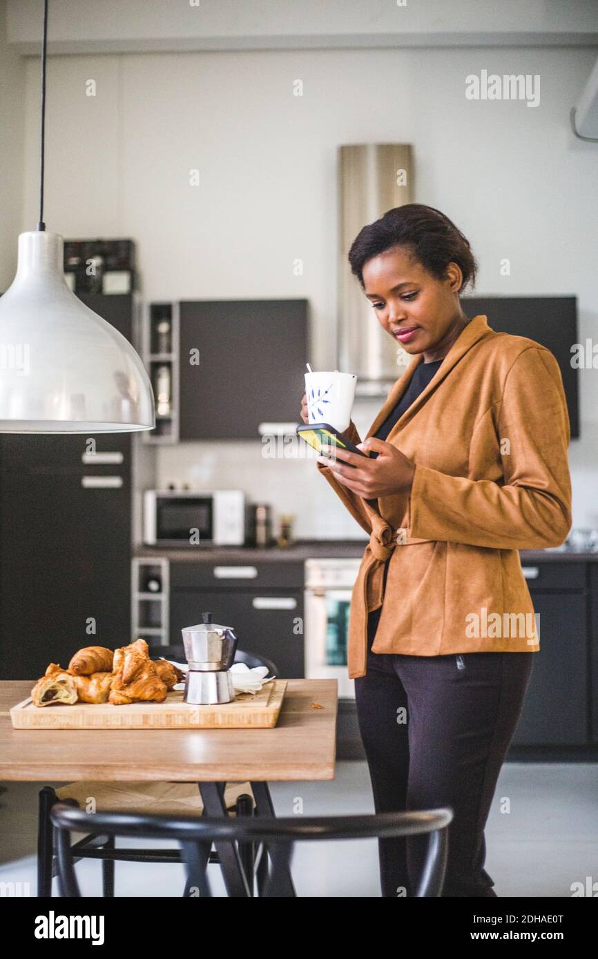 Confident female architect using phone while standing with coffee at home Stock Photo