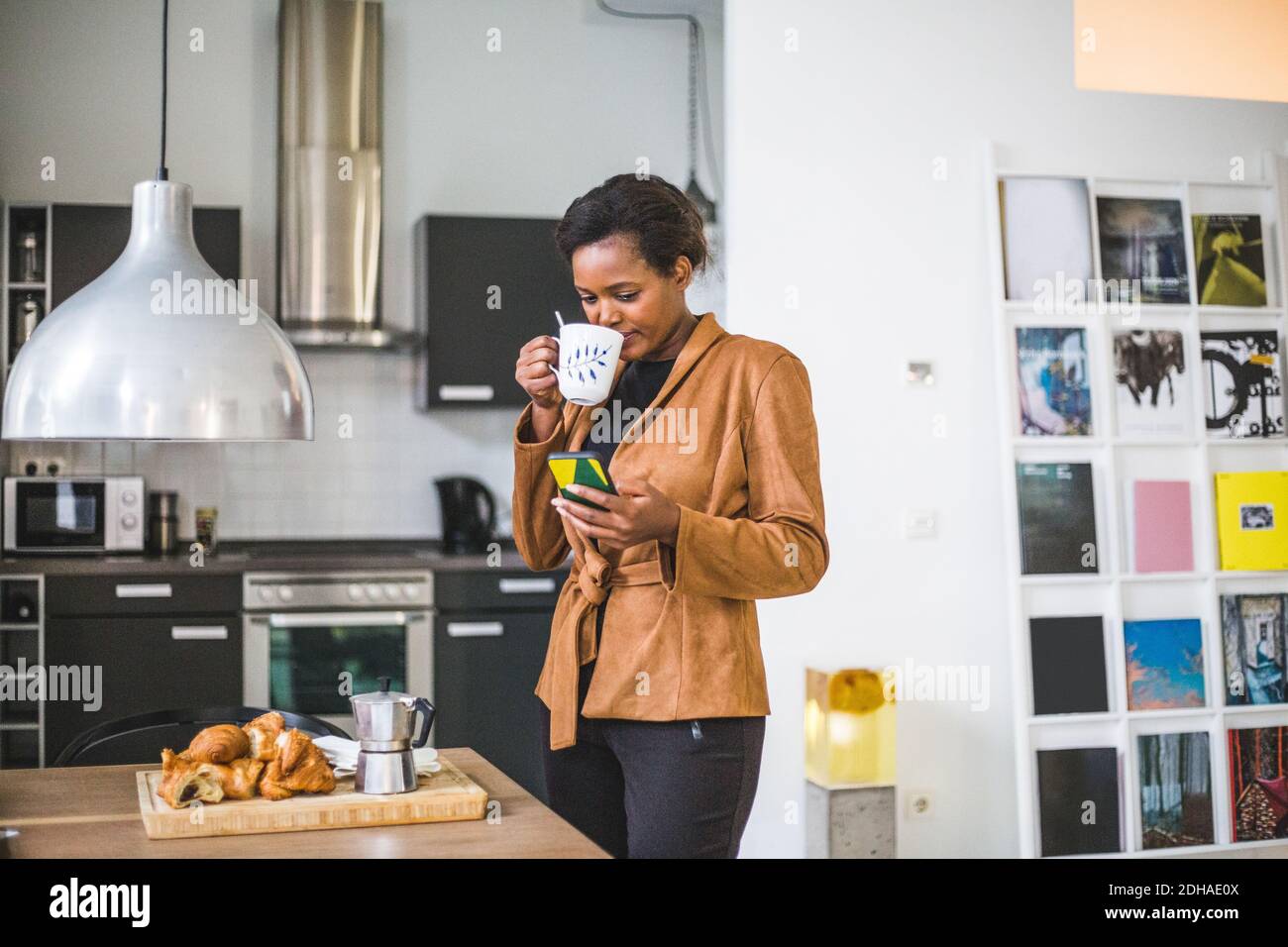 Smiling female architect drinking while using phone at home Stock Photo