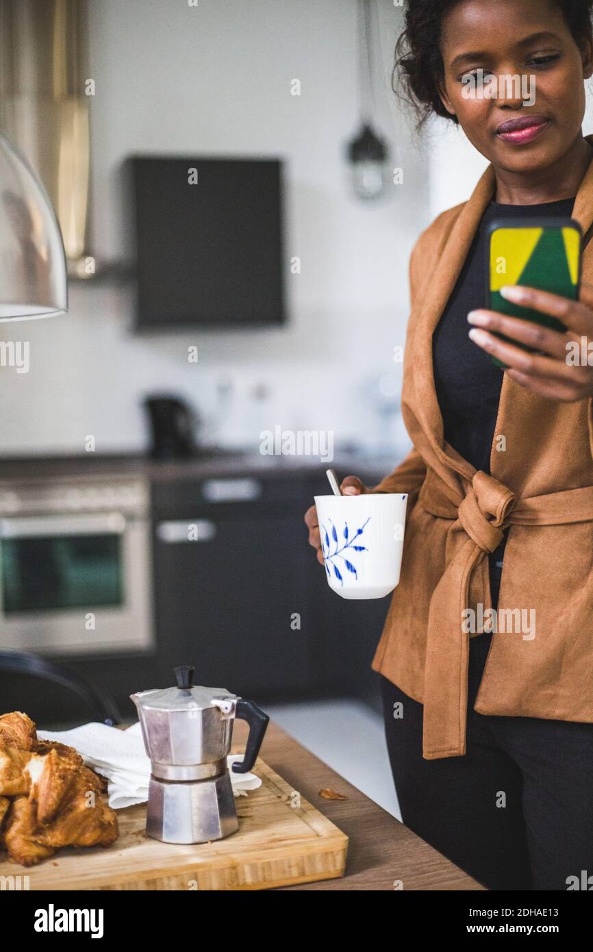 Confident female architect using phone while standing with cup at home Stock Photo