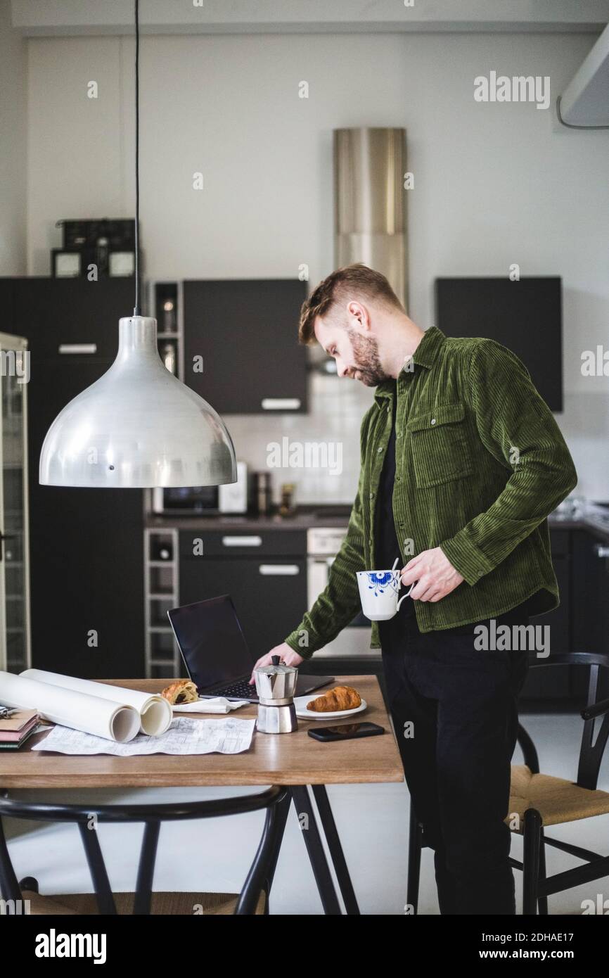 Male architect using laptop while standing with cup by table Stock Photo