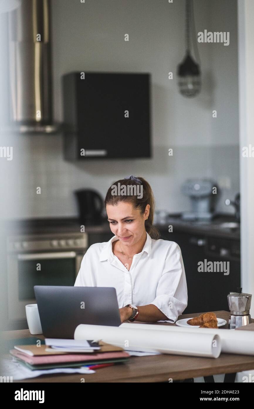 Smiling female freelancer using laptop while sitting by table at home Stock Photo