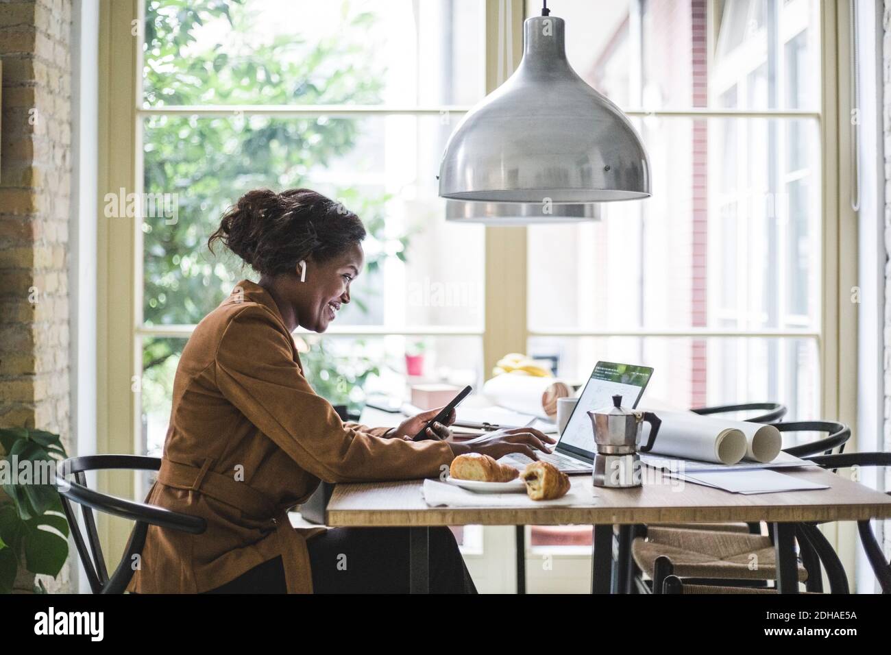 Smiling female architect using phone while sitting at home office Stock Photo