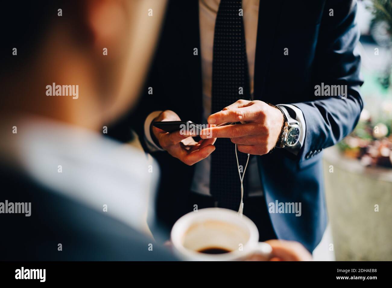 Midsection of businessman using smart phone while standing with colleague drinking coffee at cafe Stock Photo