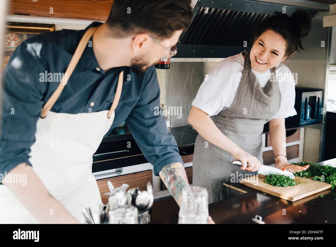 Smiling female entrepreneur cutting vegetable while working with male partner in commercial land vehicle Stock Photo