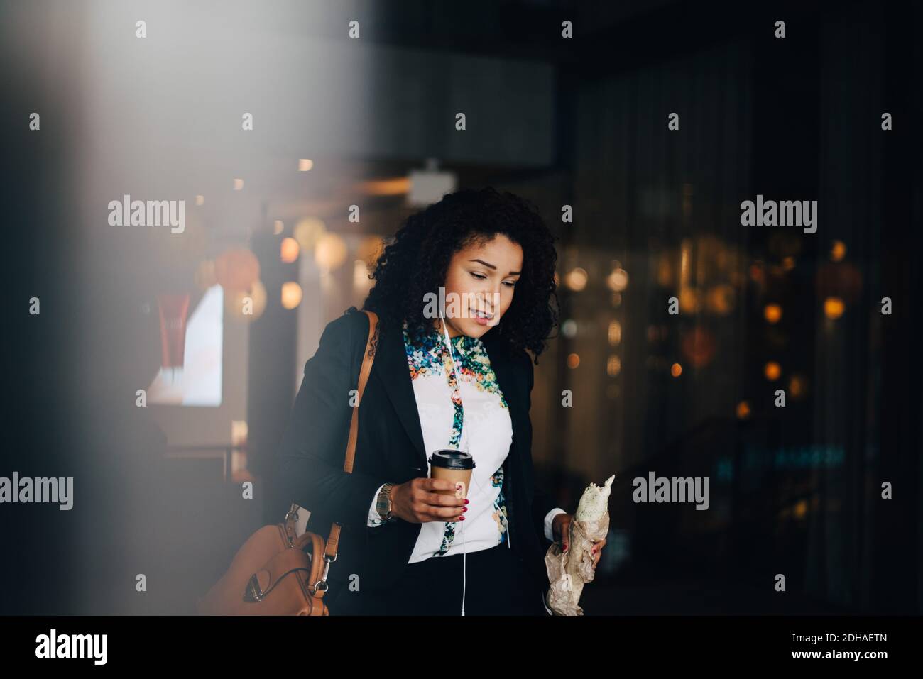 Mid adult businesswoman holding food and drink while walking in cafe Stock Photo