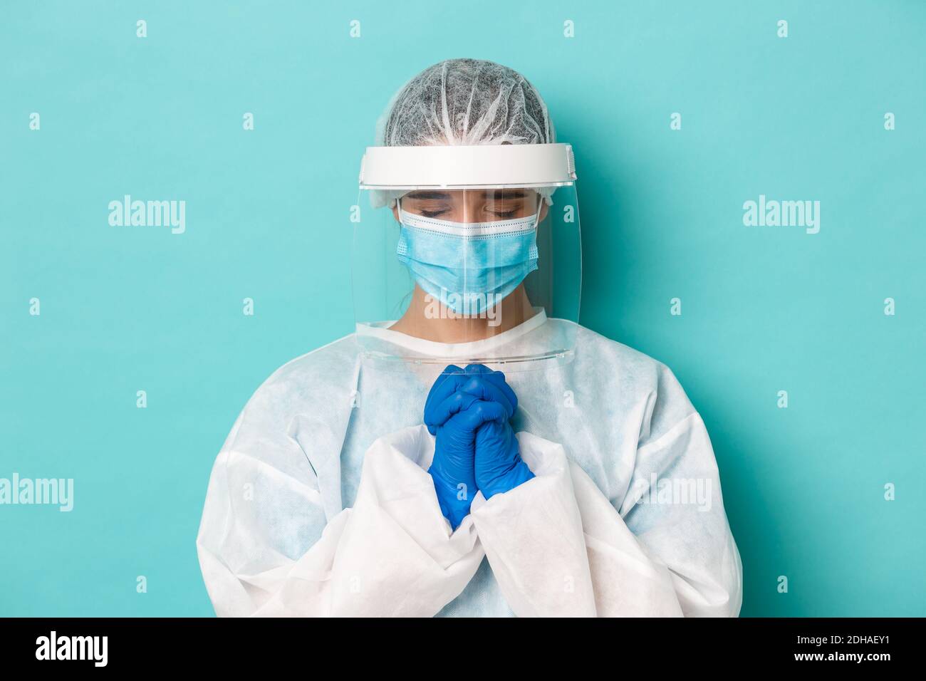 Concept of covid-19, pandemic and quarantine. Close-up of hopeful female doctor in personal protective equipment, holding hands Stock Photo