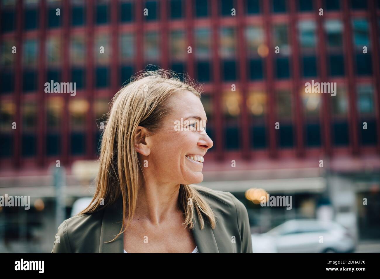 Smiling mature businesswoman looking away against building in city Stock Photo