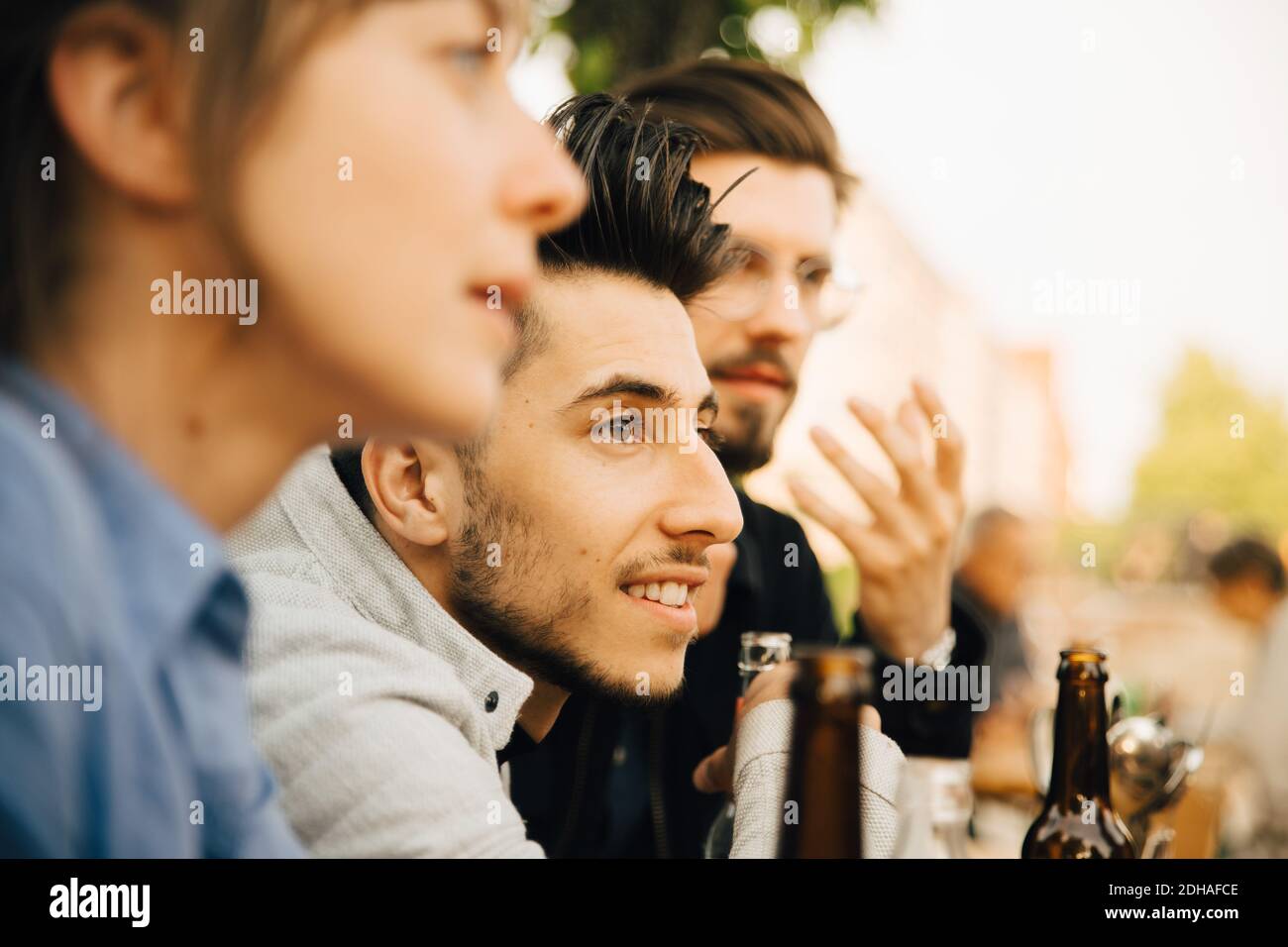 Smiling man sitting by male and female friend at social gathering Stock Photo