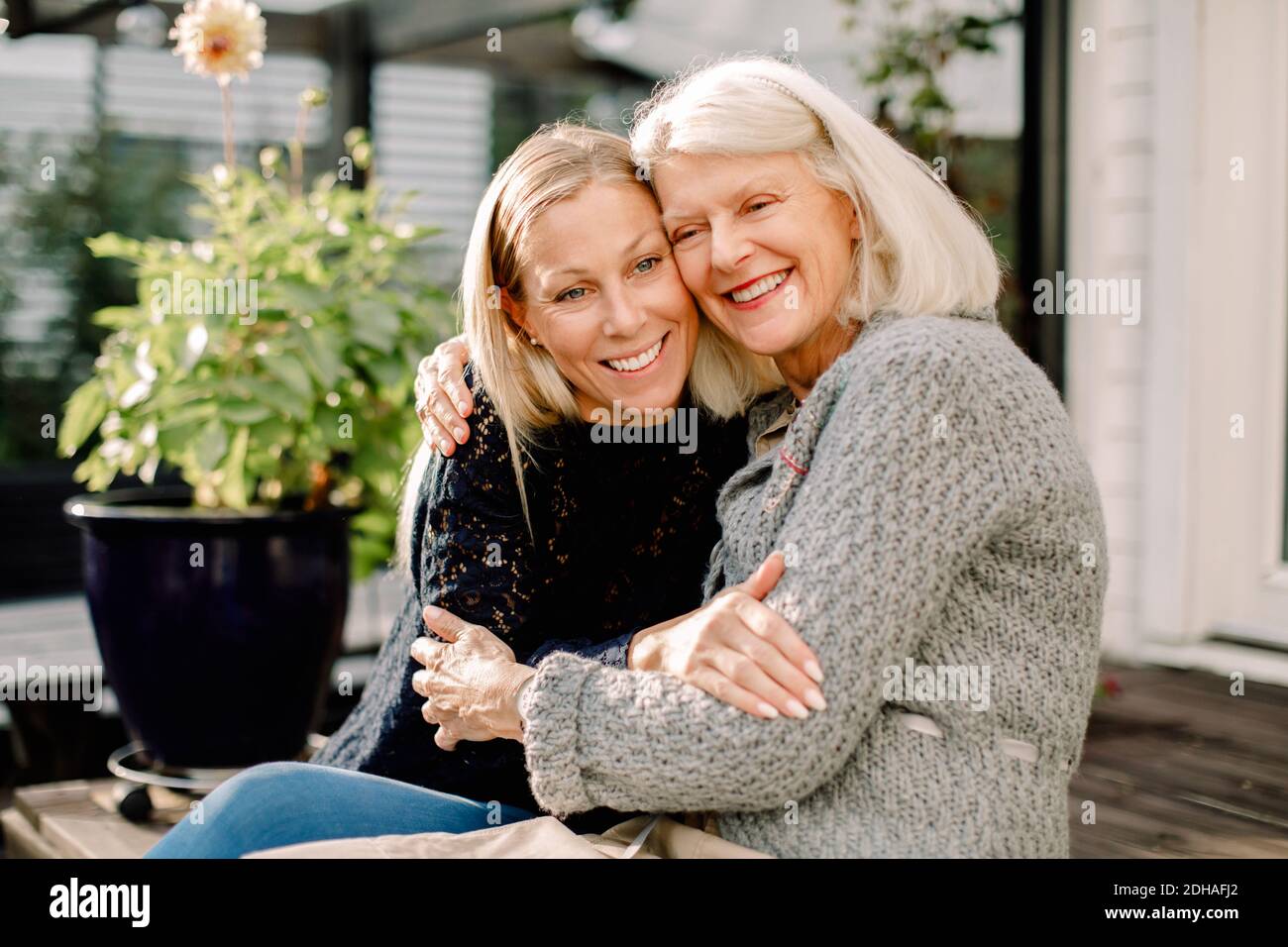 Smiling mother and daughter with arm around sitting in backyard Stock Photo