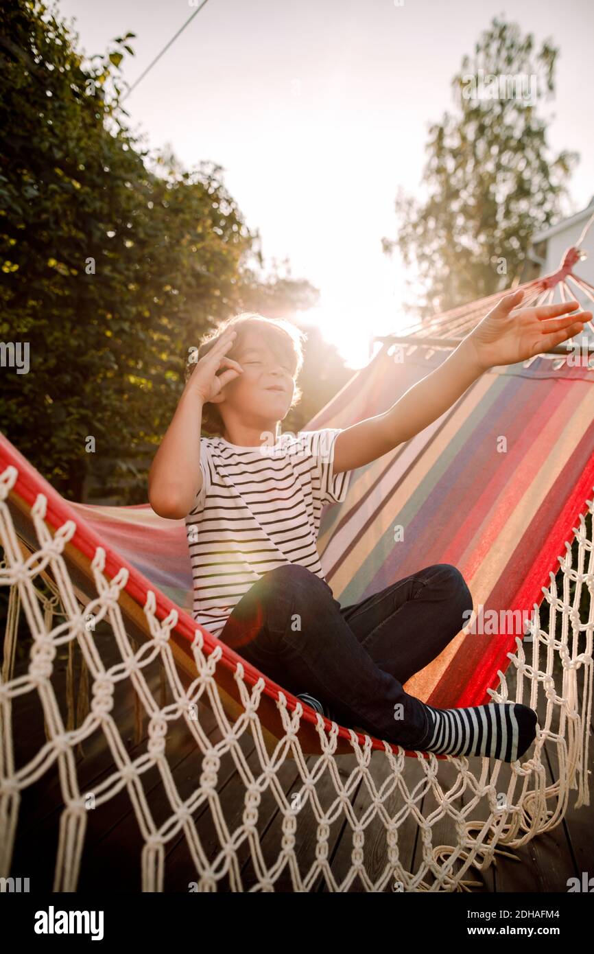 Full length of boy sitting in hammock at backyard against sky Stock Photo