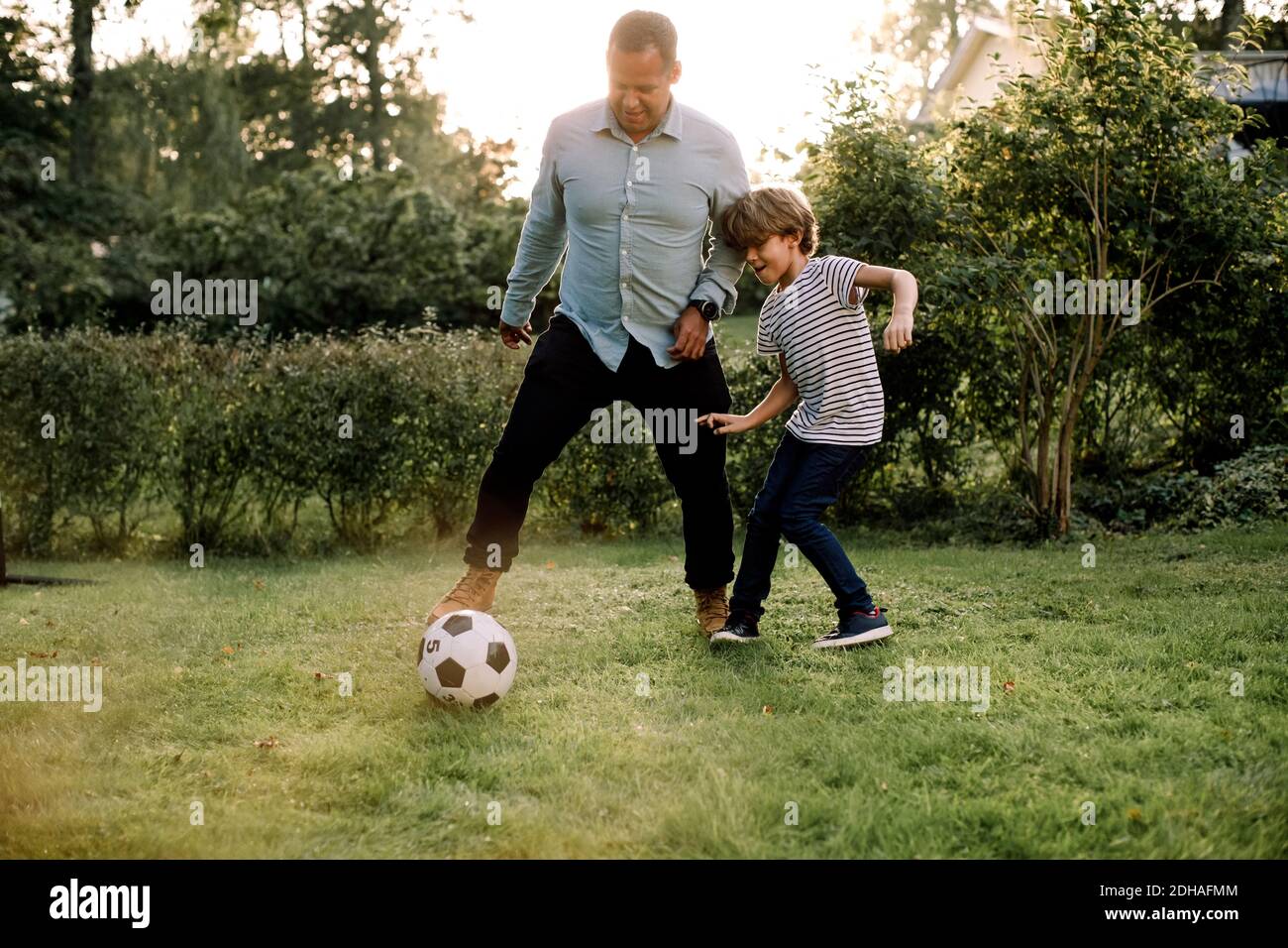 Full length of father and son playing soccer in backyard during weekend activities Stock Photo