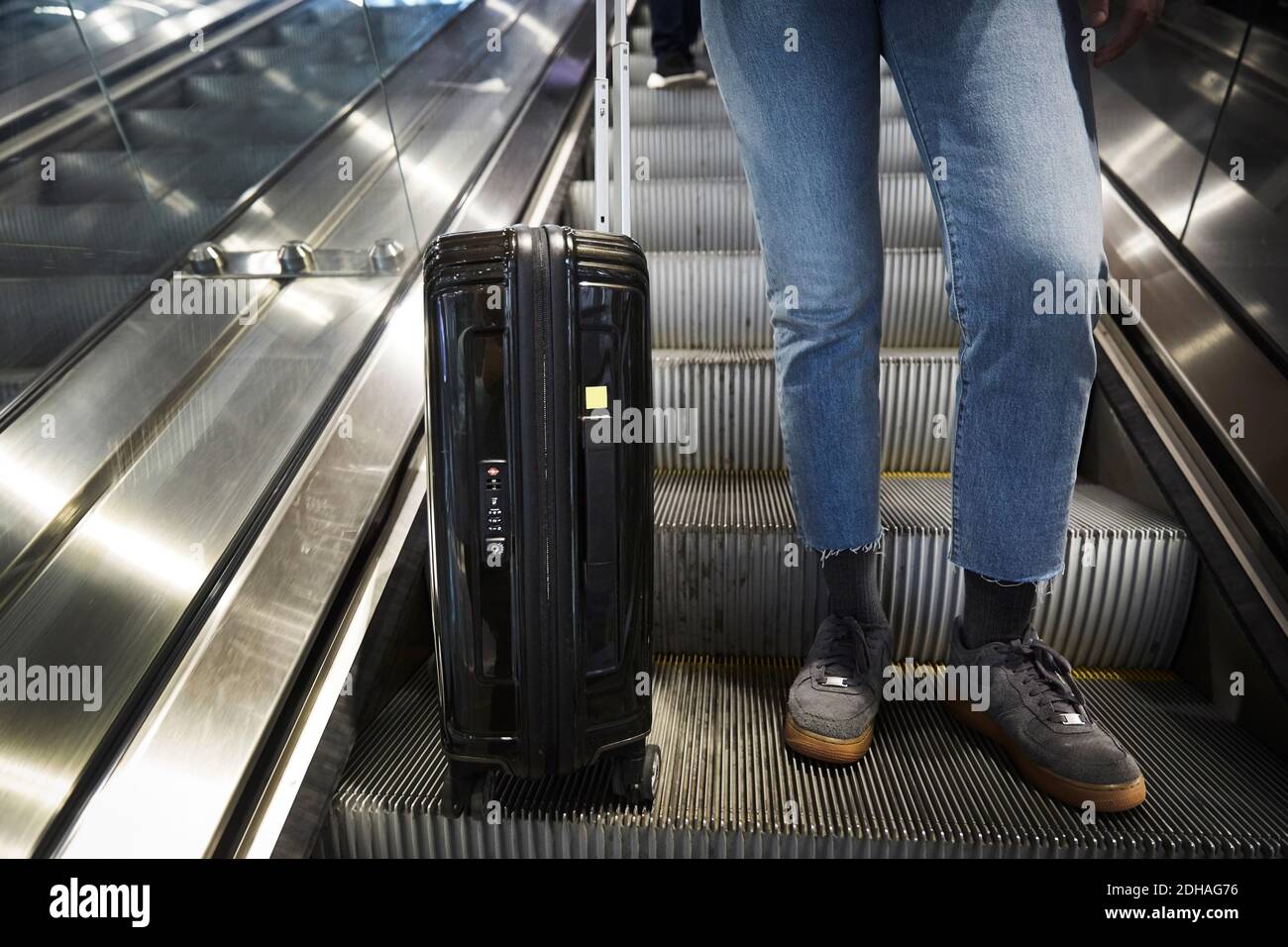 Low section of woman with wheeled suitcase standing on escalator at underground station Stock Photo