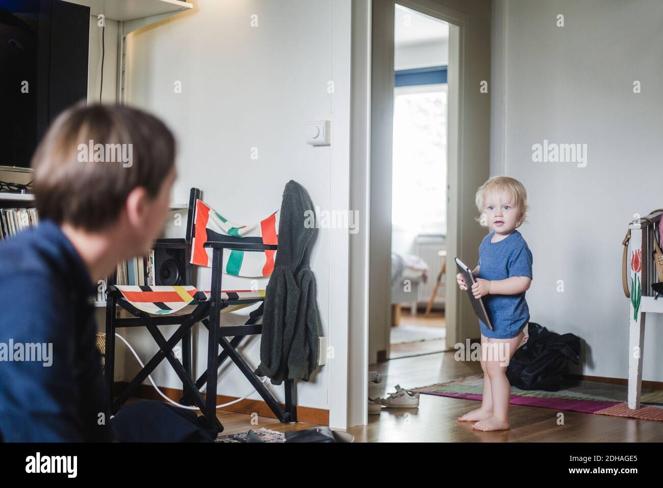 Full length of baby boy holding digital tablet while looking at father in living room Stock Photo
