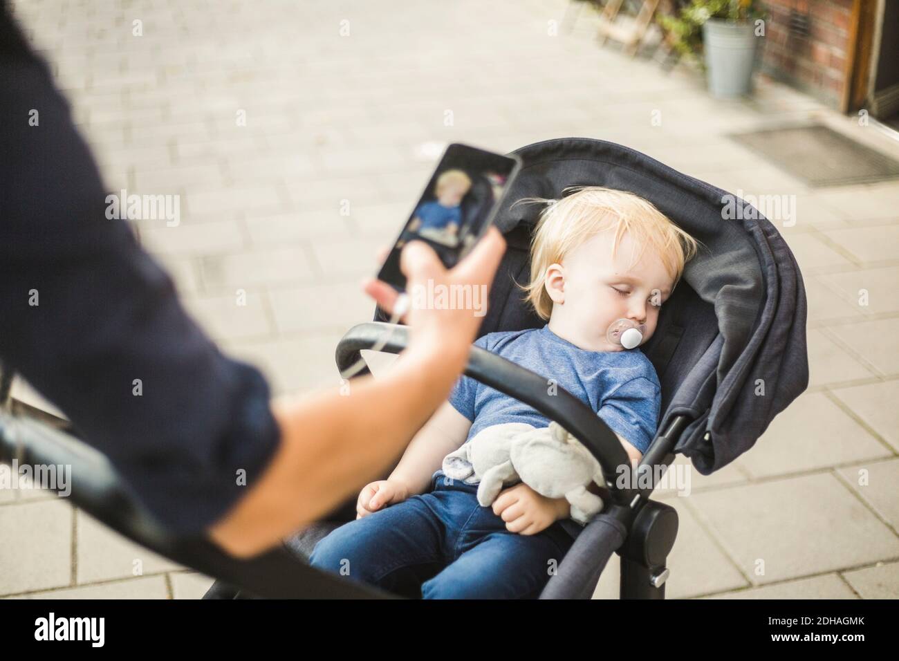 Hand of father photographing sleeping son on baby stroller in city Stock Photo