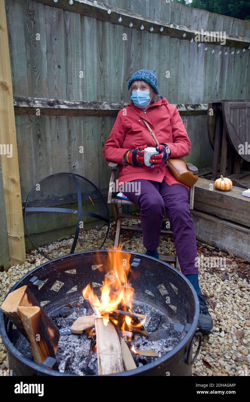 Woman wearing face mask sat around fire pit Stock Photo
