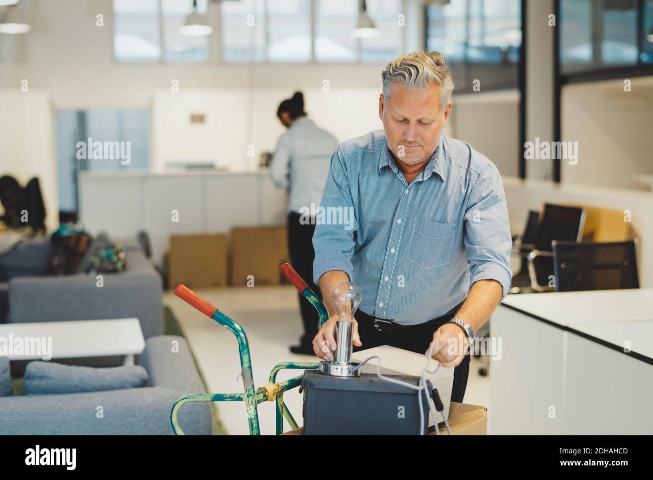 Mature businessman arranging desk lamp on box in new office Stock Photo