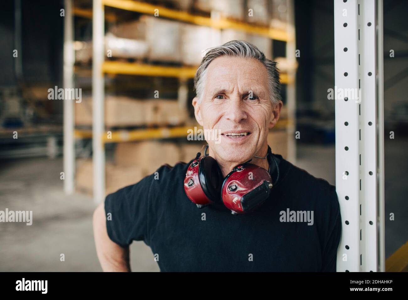 Portrait of smiling senior worker leaning on rack at industry Stock ...