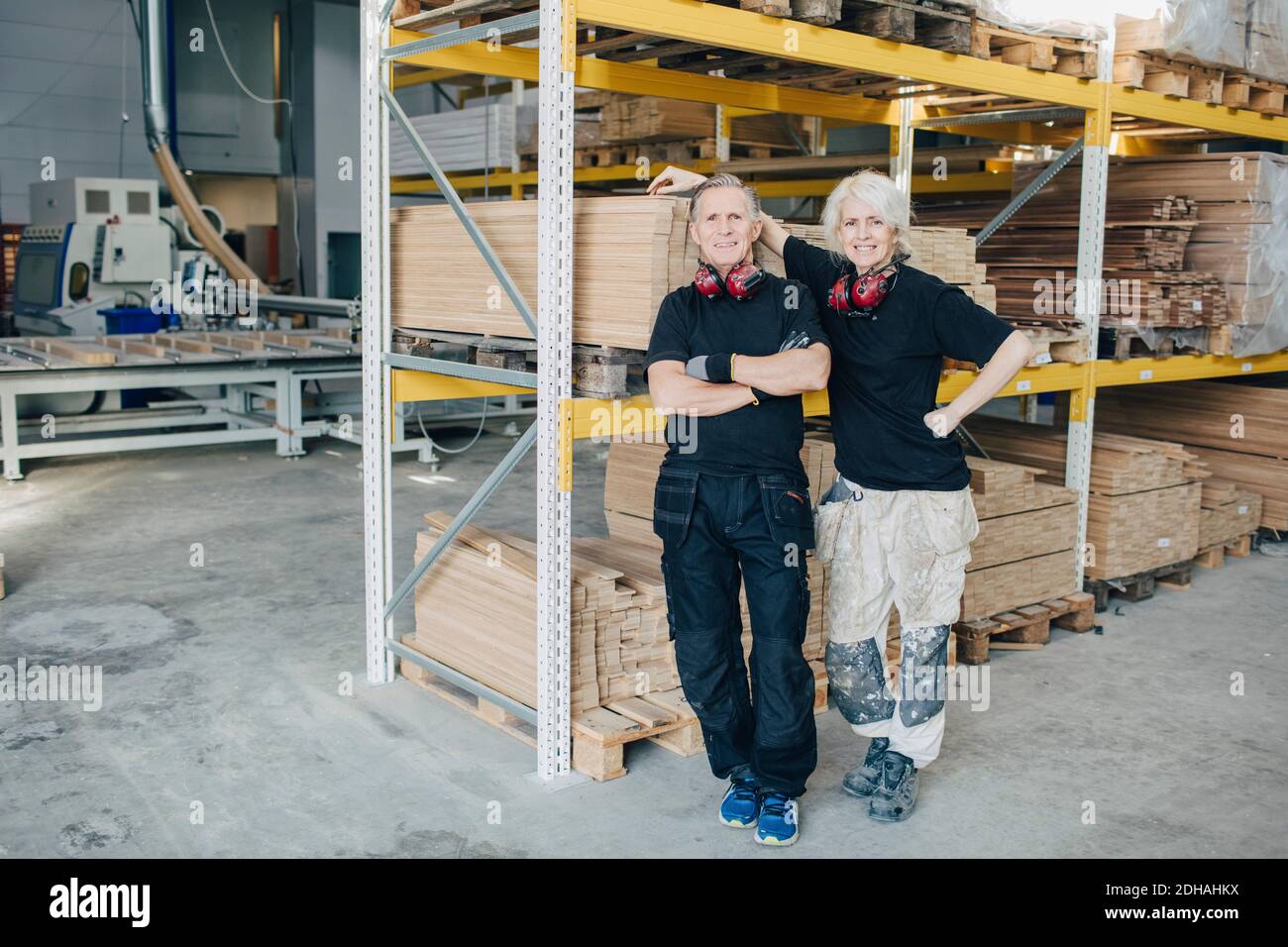Full length portrait of smiling workers standing by rack in industry ...