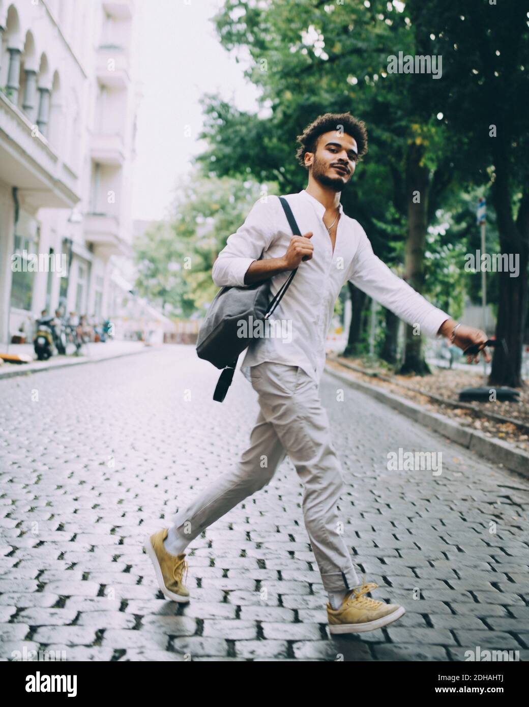 Full length of young man carrying backpack while walking on cobbled street in city Stock Photo