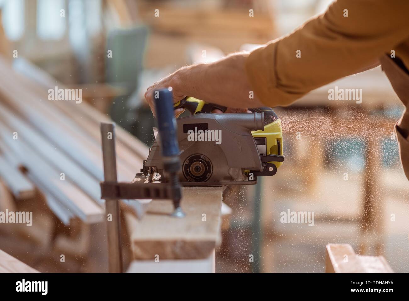 Carpenter sawing wooden bars with cordless electric saw at the joiner's