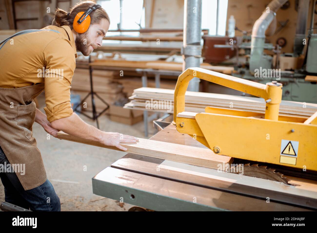 Carpentry worker sawing wooden planks with circular saw in the joinery