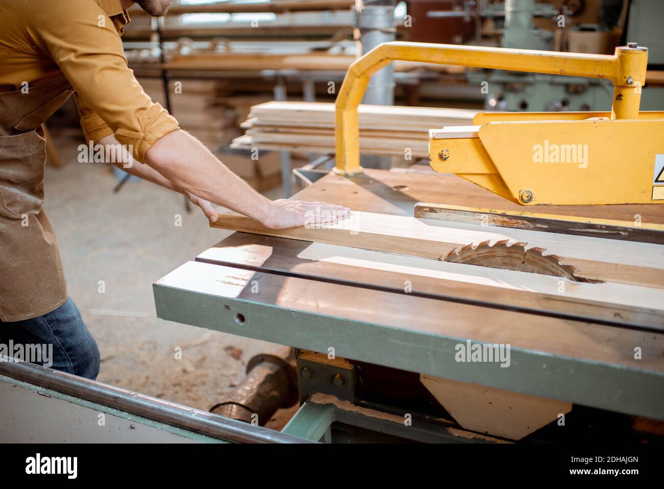 Carpentry worker sawing wooden planks with circular saw in the joinery