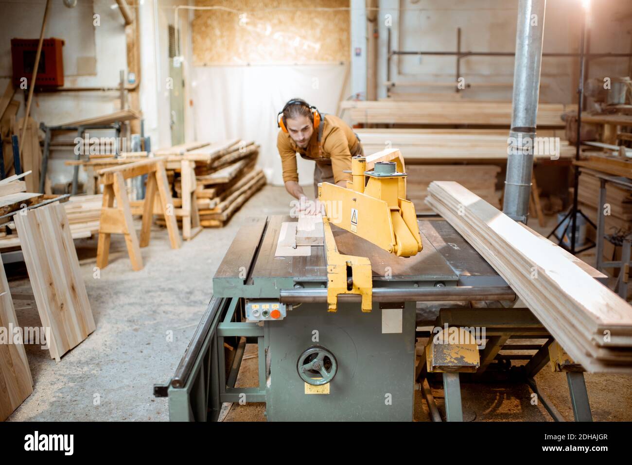 Carpentry worker sawing wooden planks with circular saw in the joinery