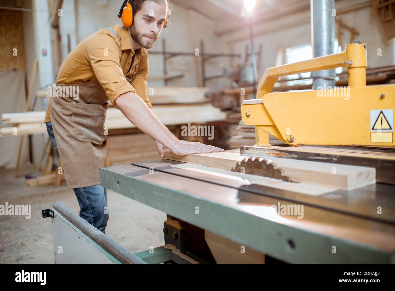 Carpentry worker sawing wooden planks with circular saw in the joinery