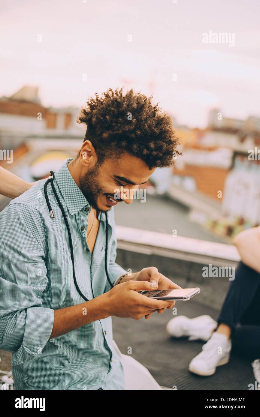 Smiling young man text messaging on smart phone at terrace party Stock Photo