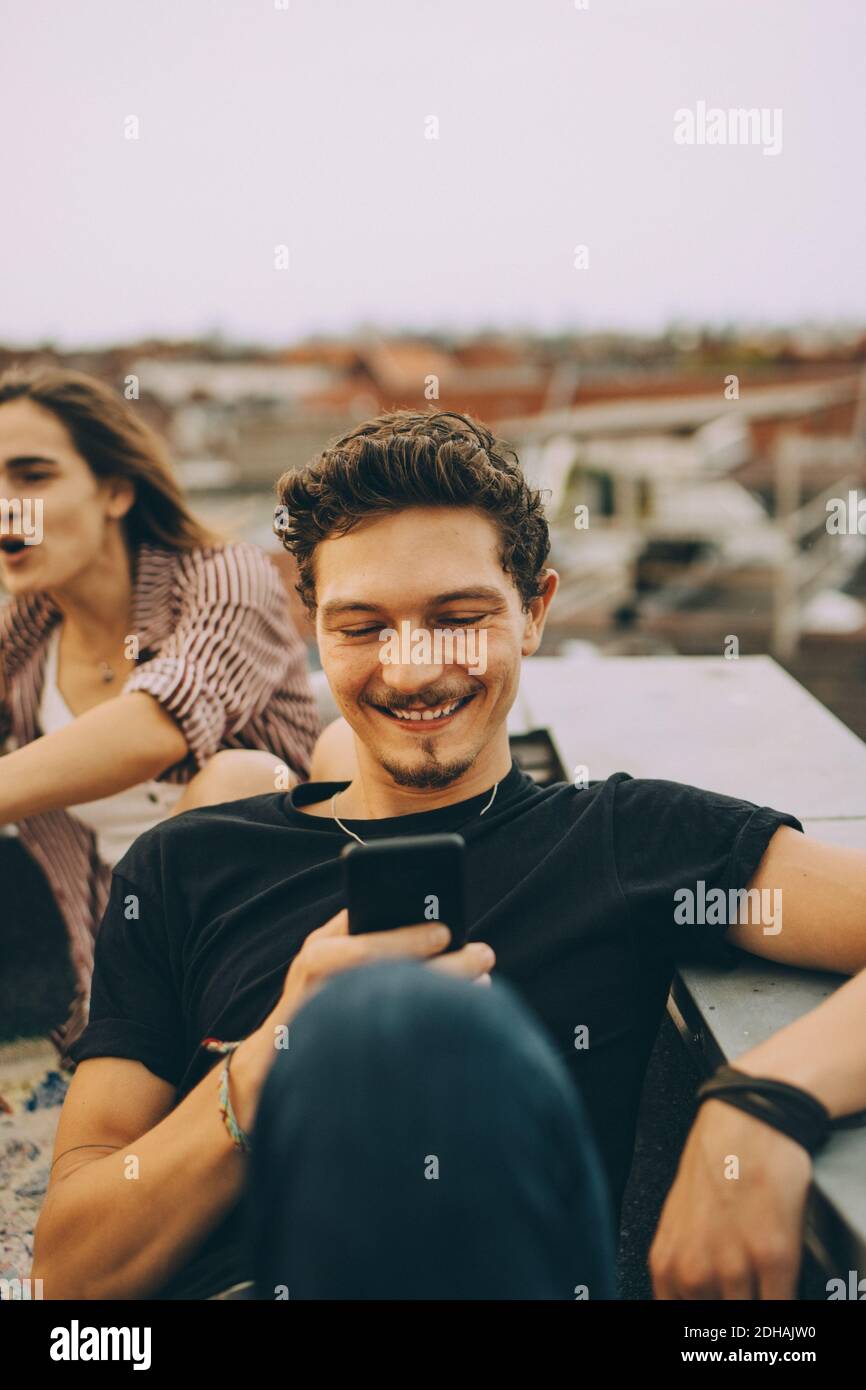 Young man using smart phone while friend enjoying at rooftop party Stock Photo