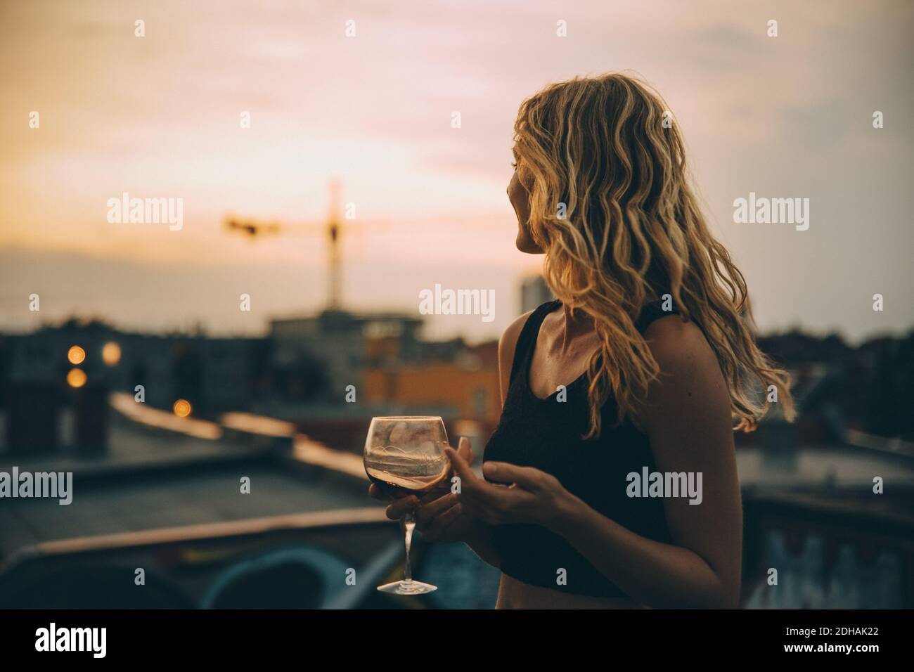 Thoughtful young woman having wine while looking away on terrace during rooftop party at sunset Stock Photo