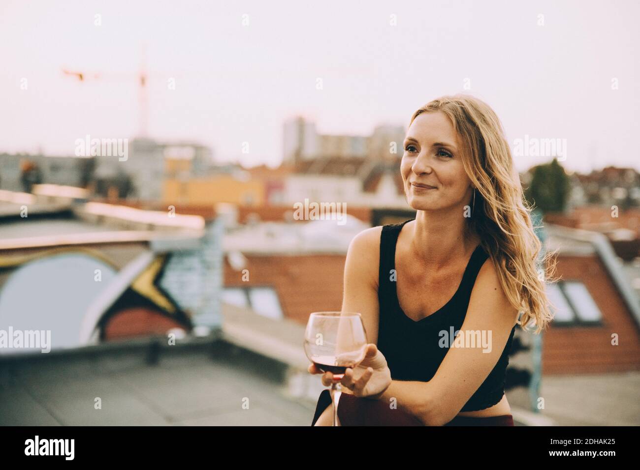 Thoughtful smiling woman having wine while sitting on terrace during rooftop party Stock Photo