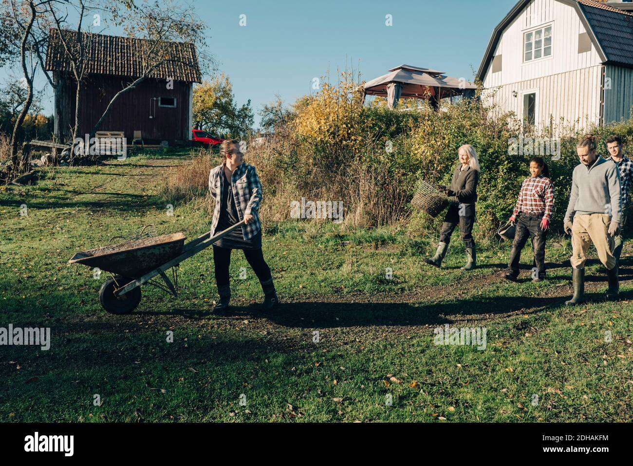 Female farmer with wheelbarrow looking at friends at organic farm Stock ...