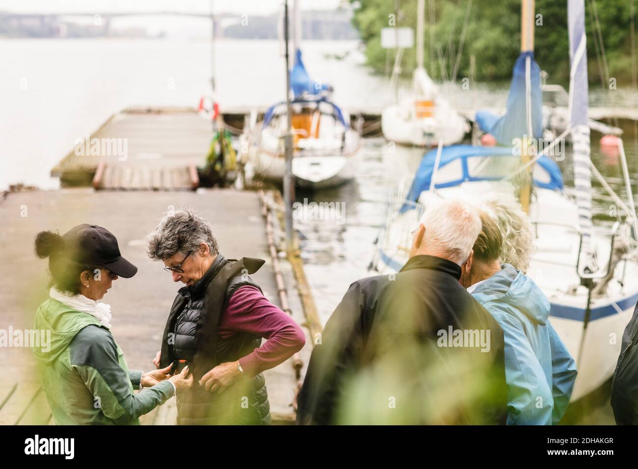Female instructor helping senior men and woman about life jacket during boat master course Stock Photo