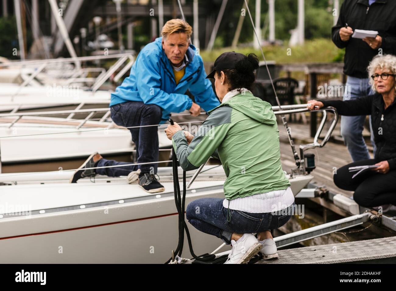 Senior man and woman looking at female instructor tying rope on railing of yacht during boat master course Stock Photo