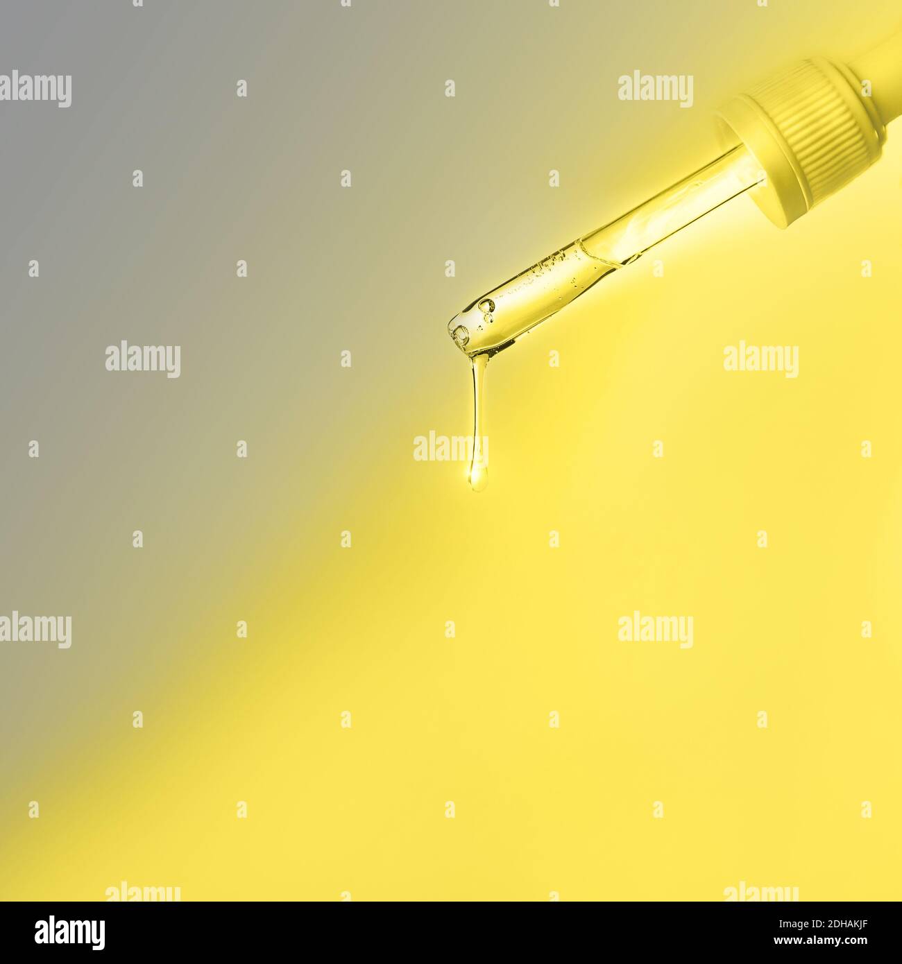 Pipette with drop of serum or hyaluronic acid on bright illuminating yellow and gray natural