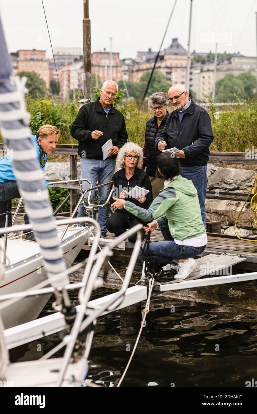 Senior men and women listening to female instructor by yacht during boat master course Stock Photo