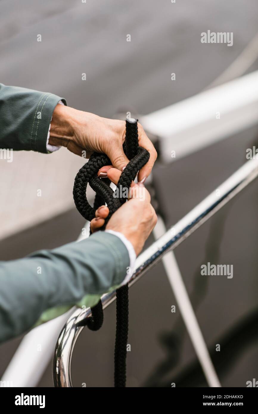 Cropped hands of senior female instructor tying rope on yacht's railing Stock Photo
