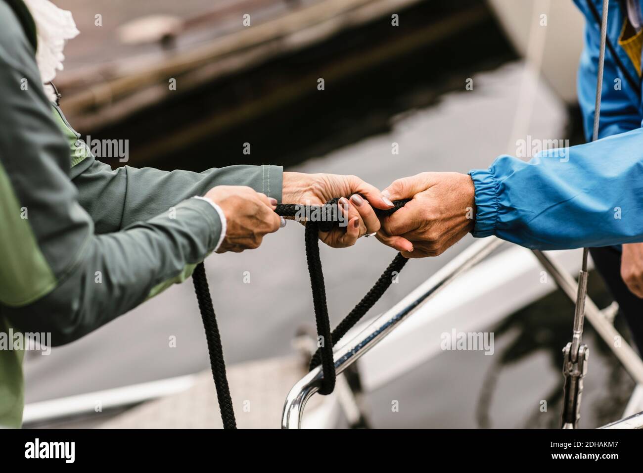 Cropped hands of female instructor and senior man tying rope on yacht's railing Stock Photo