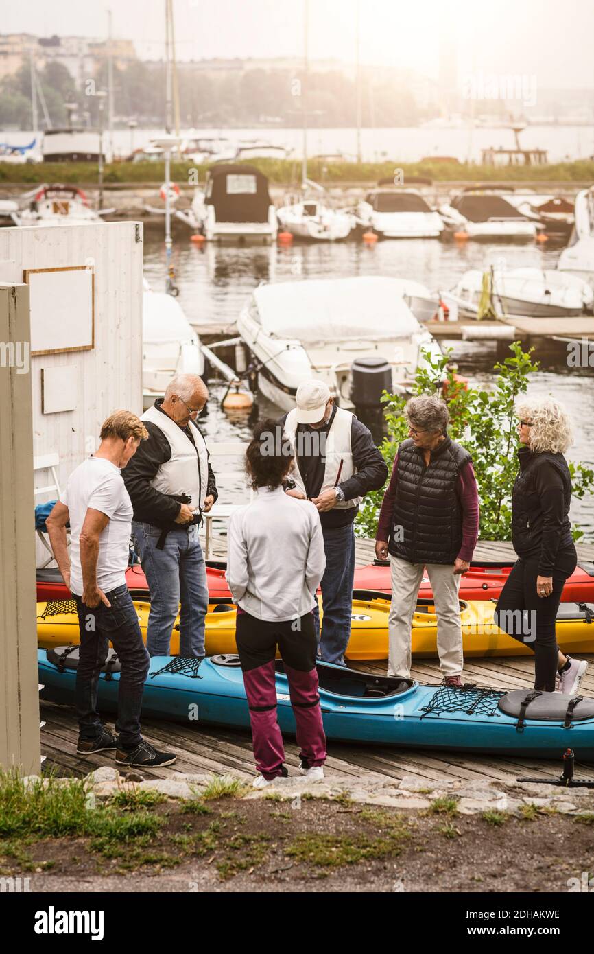 Senior men and women looking at male instructor wearing life jacket while standing by kayaks Stock Photo