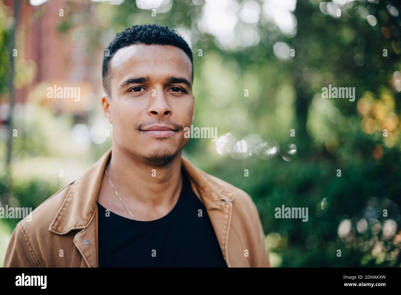 Close-up portrait of man wearing brown jacket standing by plant Stock Photo